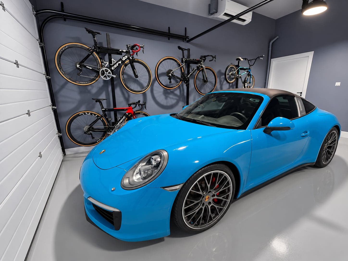 The finished Villa G28 garage: six bikes on custom wall racks, split air-conditioning unit, epoxy floor and a sports car parked inside