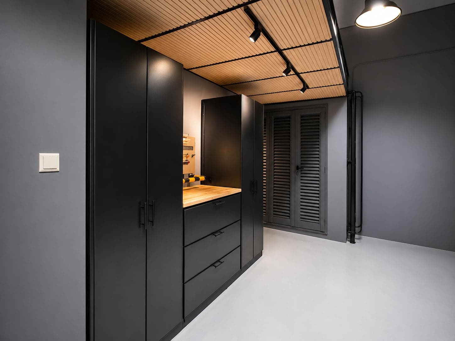 Gloss black cabinets with a timber workbench under a slatted timber mezzanine soffit with track lighting