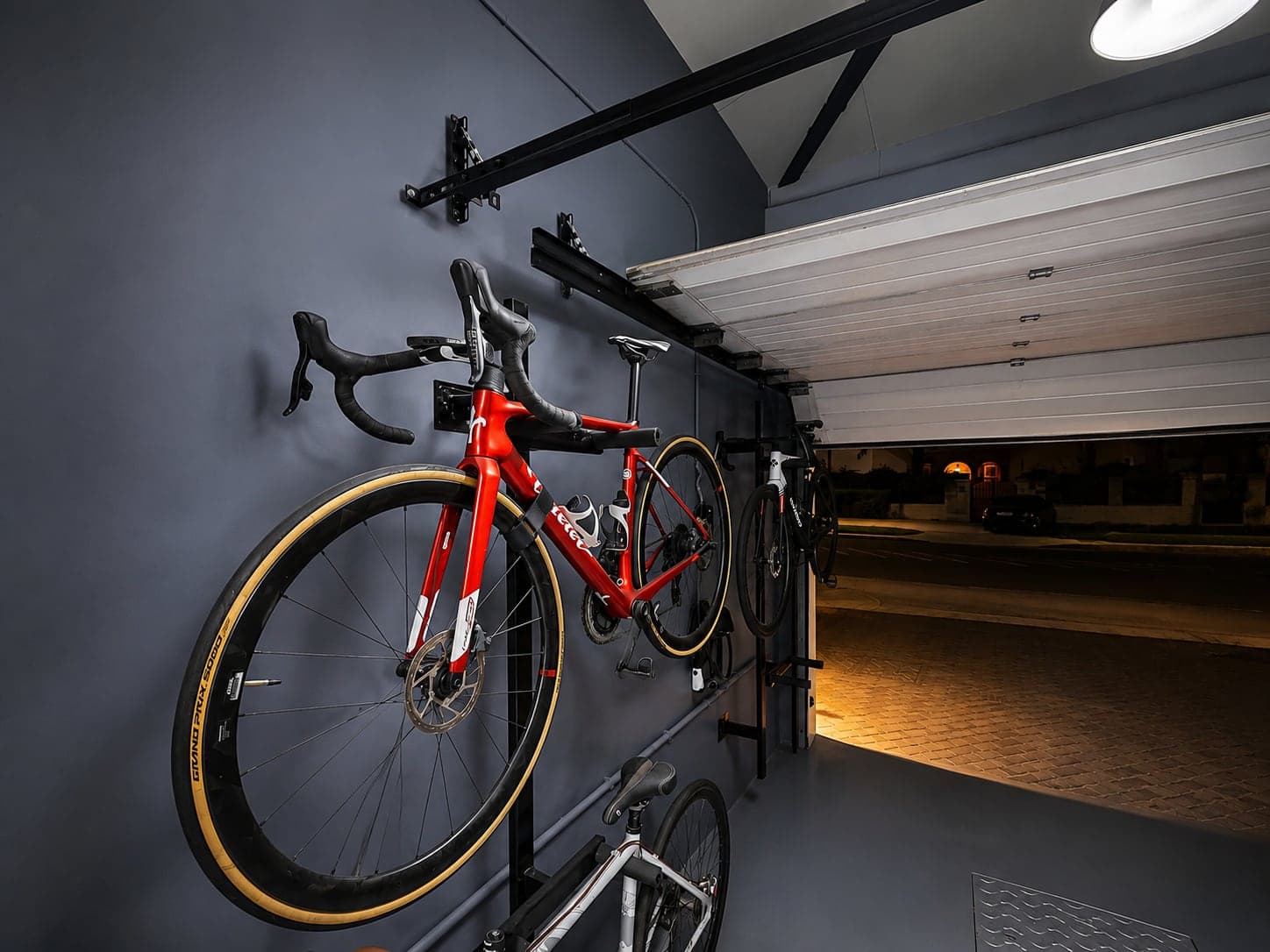 Road bikes on wall racks with the open garage door and lit driveway beyond