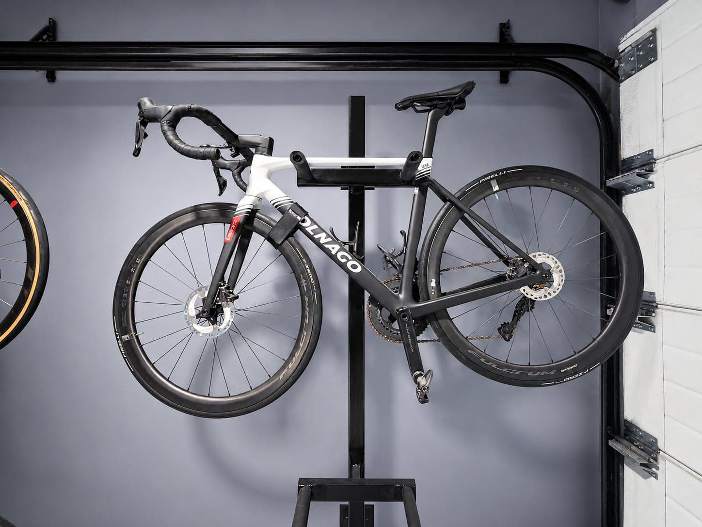 Colnago road bike hung on a custom welded steel wall rack in the G28 garage